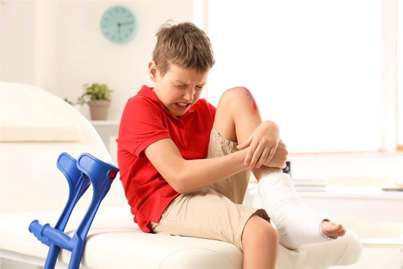 Little boy with wounded knee from slip and fall sitting on couch in clinic.